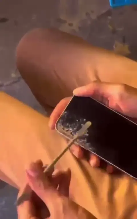 Mãos removendo vidro estilhaçado de um iPhone com uma ferramenta de abertura.